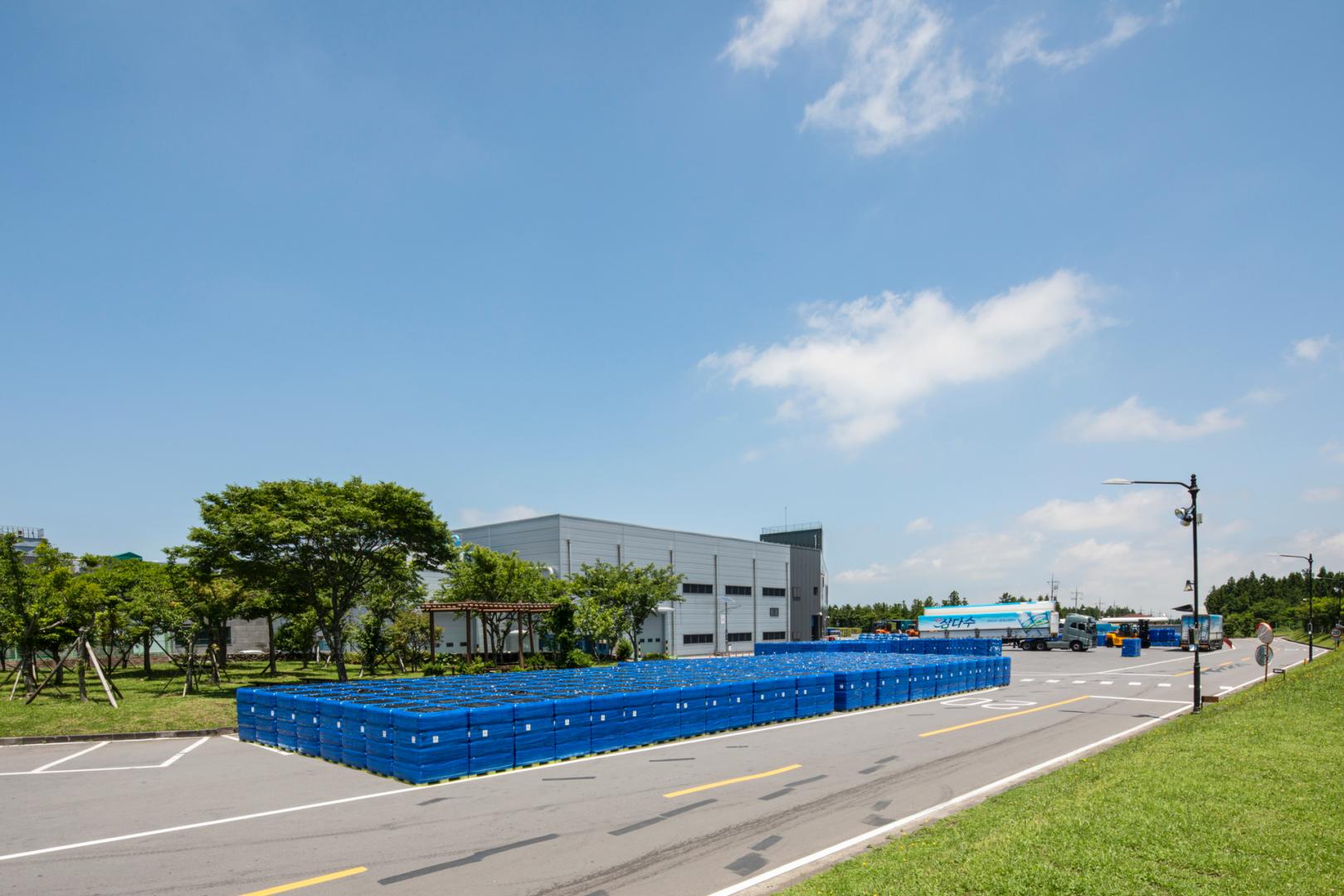 濟州三多水工廠前堆滿藍色瓶裝水棧板,三多水標誌卡車正在待命的畫面